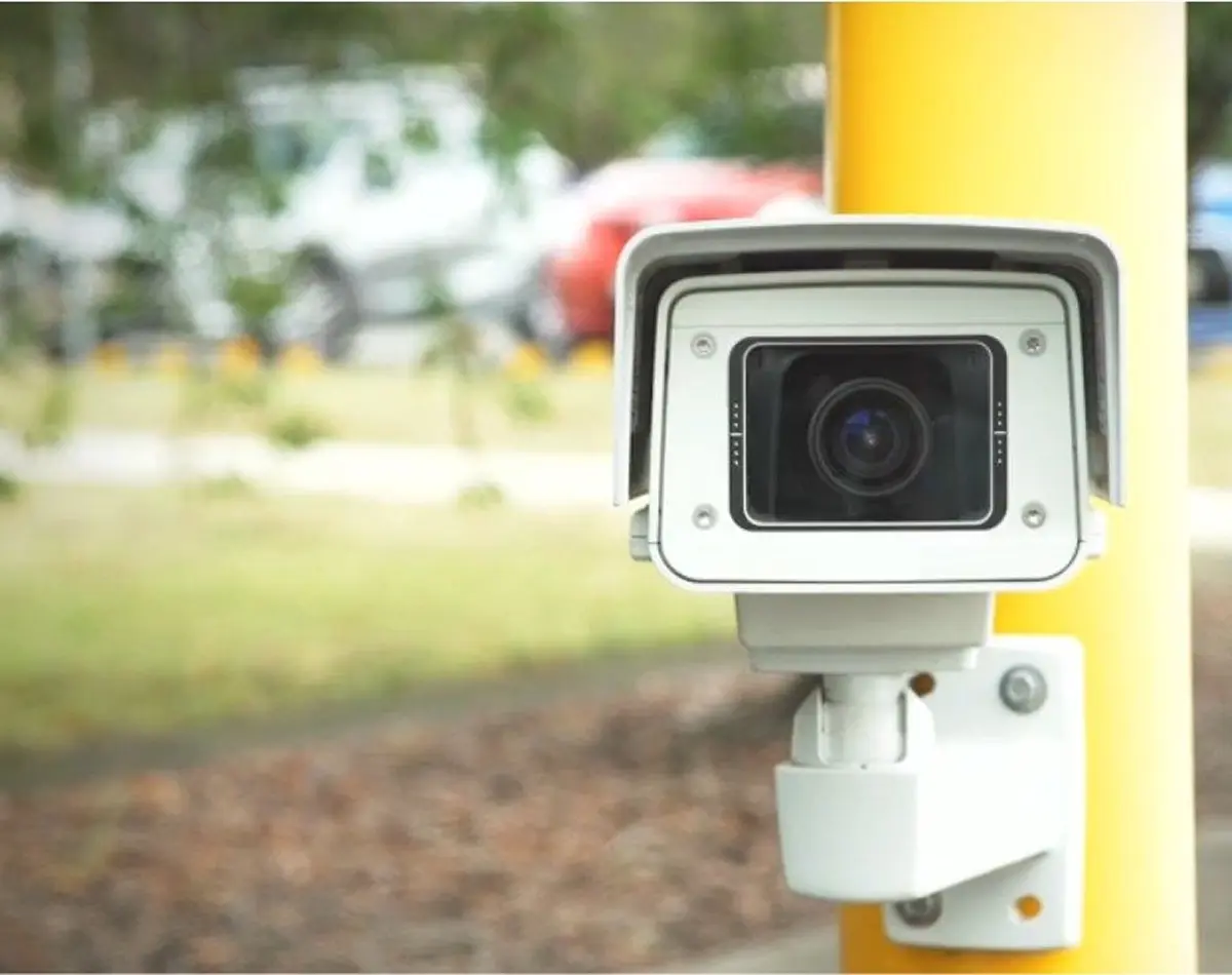 Close-up of an outdoor ANPR security and license plate recognition camera mounted on a yellow industrial pole for automated vehicle tracking